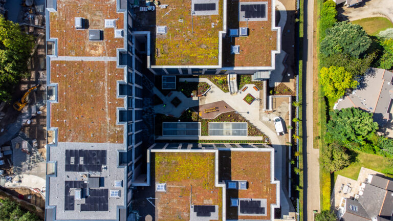 An ariel photo of the roof of a U-shaped building.The height decreases toward each end.There is a path in the middle and plants between the paths.