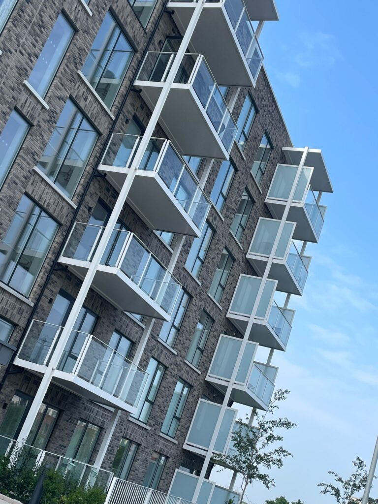 A picture of apartment blocks.They have modern grey brick work.They have white balconies with privacy screens on either side and glass banisters on the front.