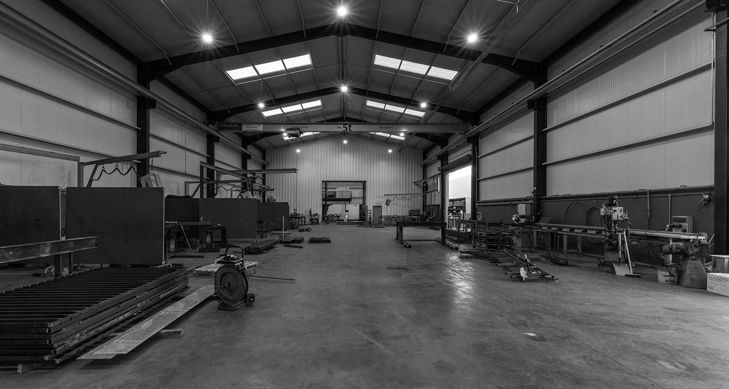 A black and white photo of a large garage.There is machinery on either side of the garage.There is a beam across the top of the garage with '5t' on it.There is bright lights on the roof.