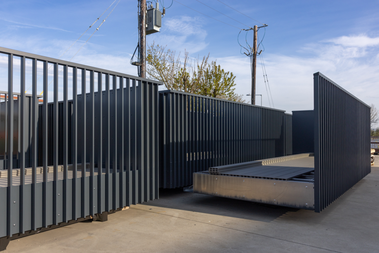 A group of dark grey container-like structures.There is gaps between each pillar of the container.It has a fence style pattern.