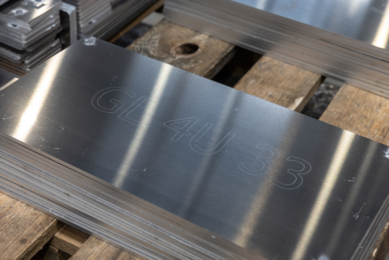 A pile of small metal sheets.The top sheet has the words 'GL 4U 33' engraved on it.