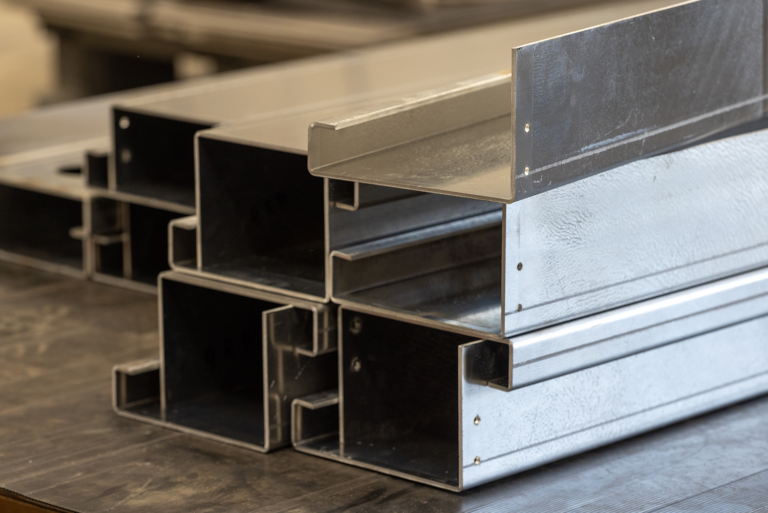 A collection of metal beams stacked on top of each other.There is 7 beams in the front, stacked in a 4,4,1formation.In the background there is more beams stacked in a similar pattern.