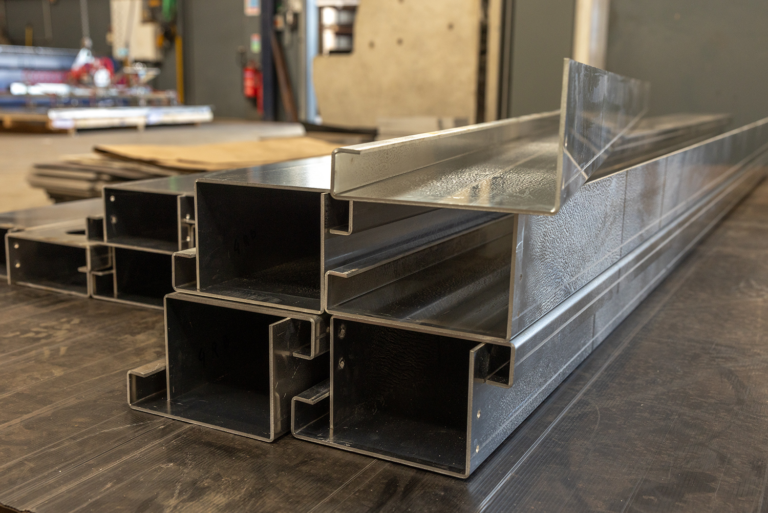 A collection of metal beams stacked on top of each other.There is 7 beams in the front, stacked in a 4,4,1formation.In the background there is more beams stacked in a similar pattern.