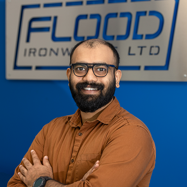 A man in a brown shirt.He has a black beard and a little hair on his head.He wears glasses.