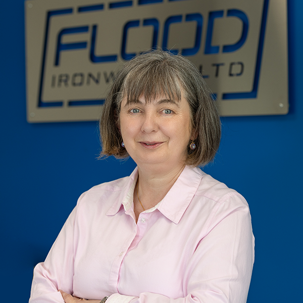 A woman with brown-grey hair.She has earings and a bob haircut.She is wearing a pink blouse.
