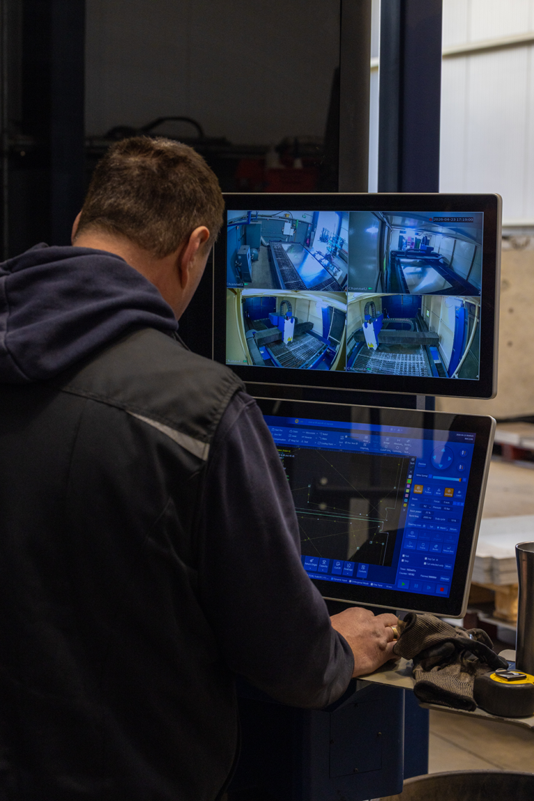 A man working on a computer to operate a machine with a sheet of metal in it.