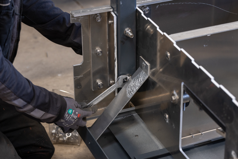 A person working on a metal structure.He is using a wrench to tighten nuts and bolts.