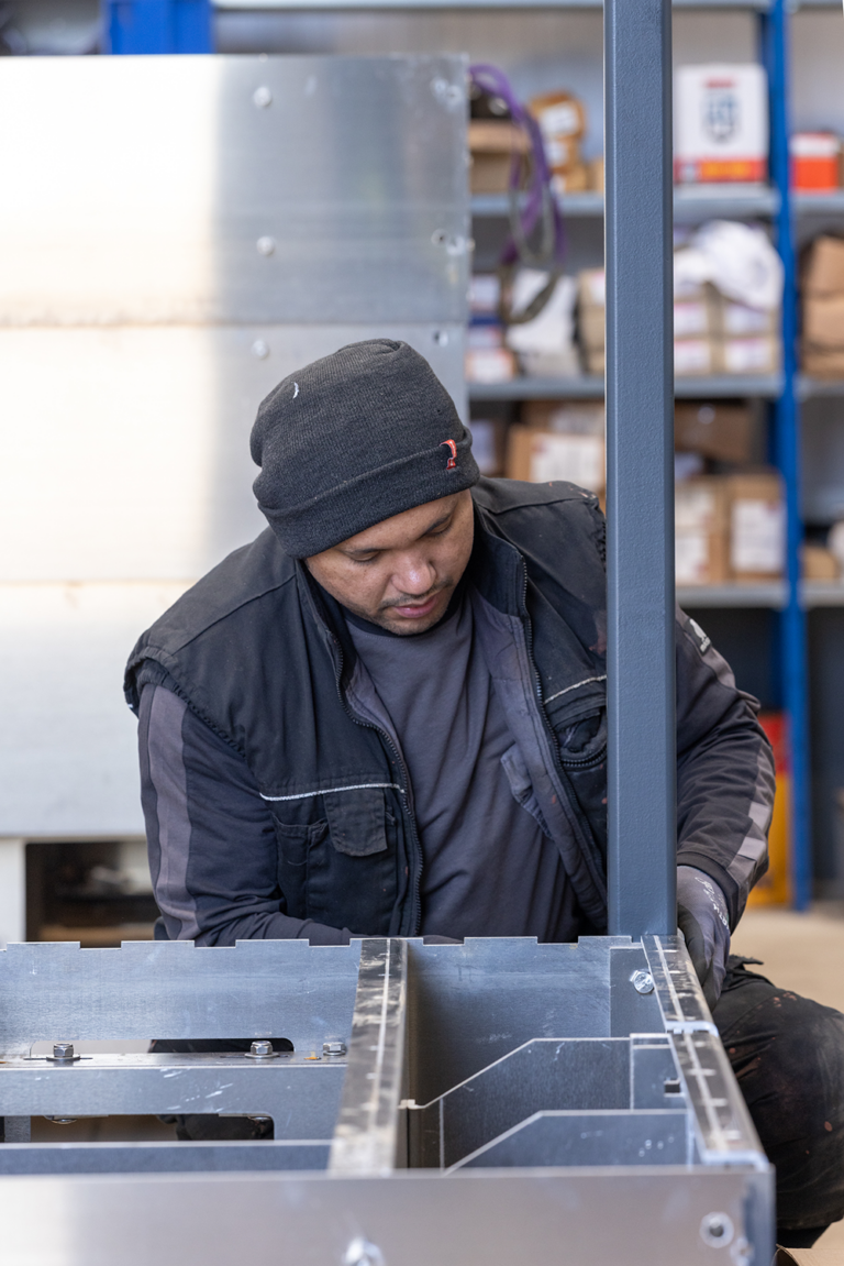 A man working on a metal frame.He is wearing a grey hat.