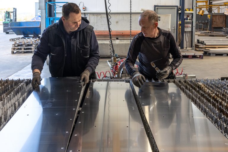 Two men working on a large sheet of metal together.