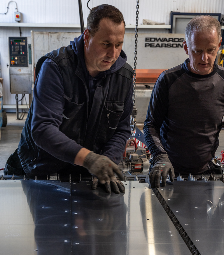 Two men working on a large sheet of metal together.