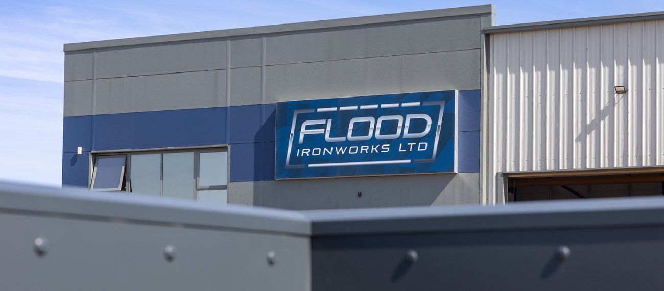 a dark grey building with a dark blue strip going across horizontally and a sign though the blue strip saying flood ironworks ltd